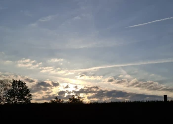 Abendhimmel mit Sonnenstrahlen und Wolken über der ländlichen Landschaft